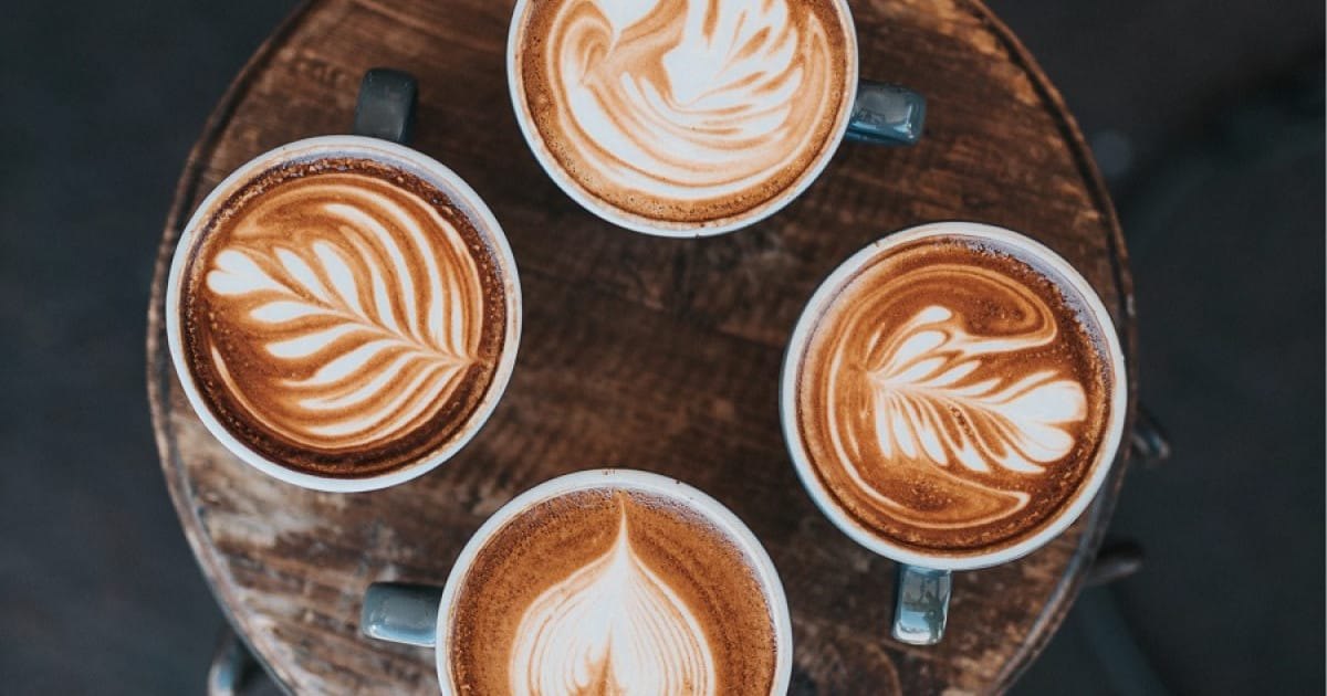 Quatre cafés latte au motif rosetta posés sur un tabouret en bois